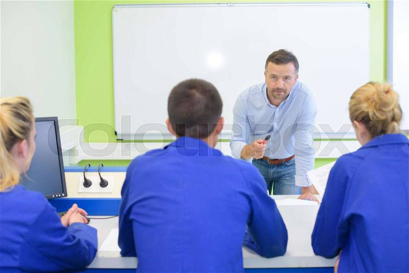 Teacher talking to pupils during technology class, stock photo