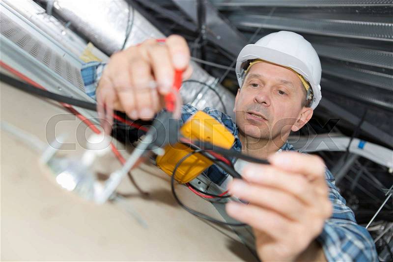Electrician repairing wiring inside office ceiling, stock photo