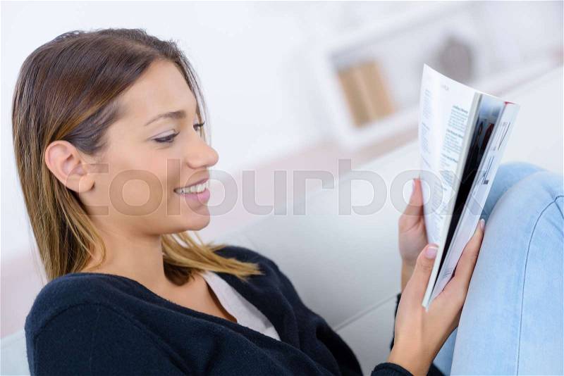 Smiling woman on couch reading at home, stock photo