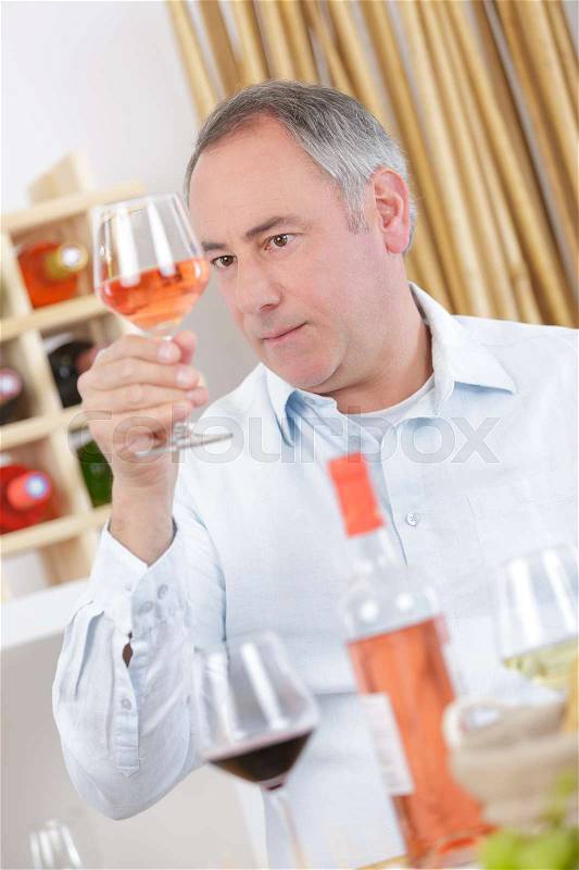 Mature man tasting glass of rose wine at home, stock photo