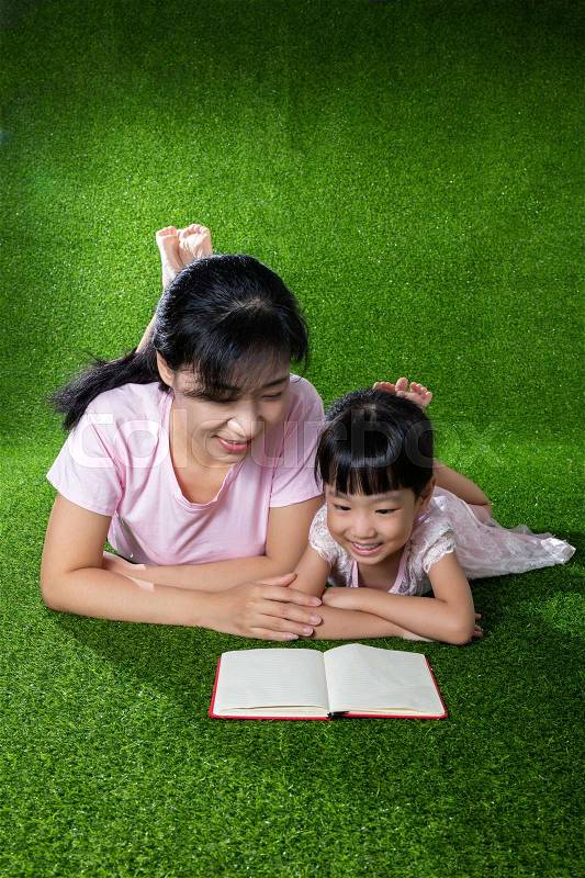 Asian Chinese mother and daughter lying on the grass and reading the book at outdoor park, stock photo