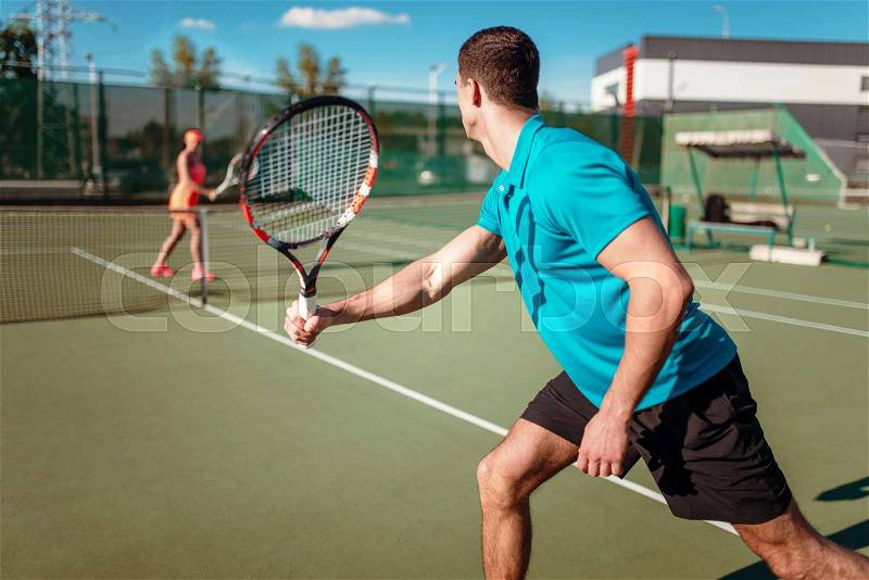 Athletic man and slim woman on tennis training on outdoor court, players with rackets. Summer season active sport game, stock photo