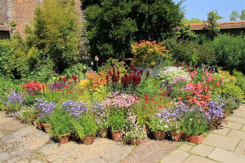 Flowerpots and boxes with many blooming flowers in different colours in one of the cottage gardens in Great Dixter House & Garden in England in the beautiful summer, stock photo