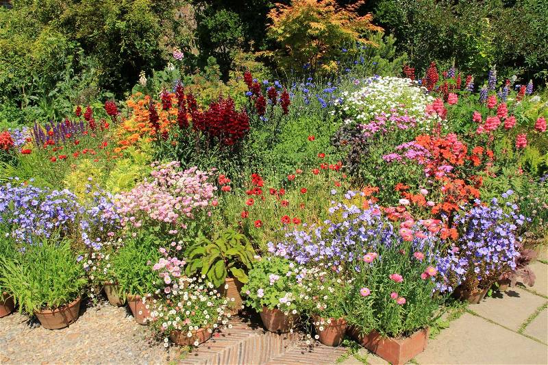 Flowerpots and boxes with many blooming flowers in different colours in one of the cottage gardens in Great Dixter House & Garden in England in the beautiful summer, stock photo
