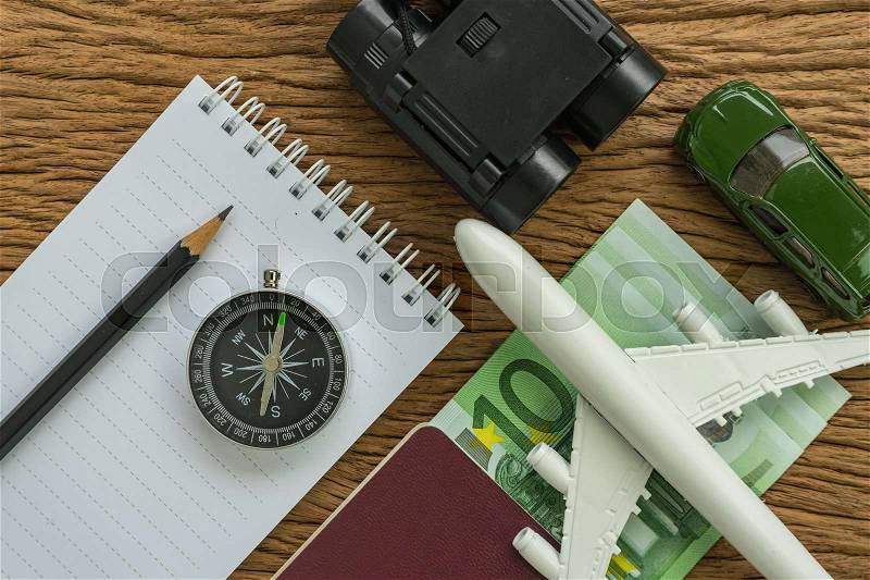 Travel planning concept with airplane, passport, compass, binoculars, pencil, paper note and Euro banknotes on wood table, stock photo