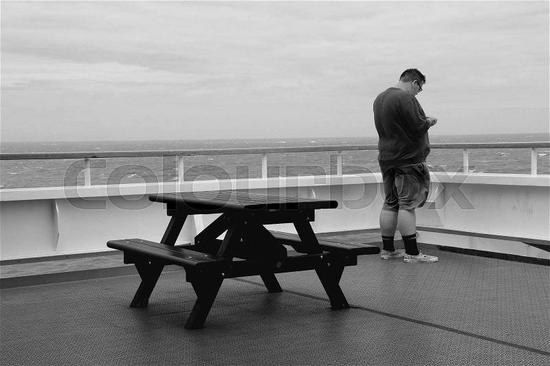 The man is busy with his mobile phone on the deck of the ferry from Dunkirk to Dover in the beautiful summer in black and white, stock photo