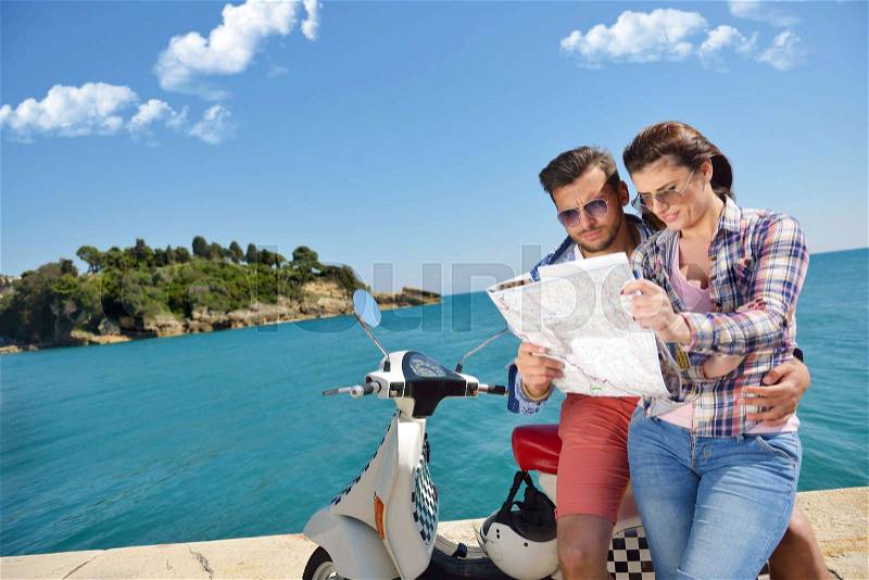 Examining map together. Beautiful young loving couple sitting on scooter together and examining map while woman pointing it and smiling, stock photo