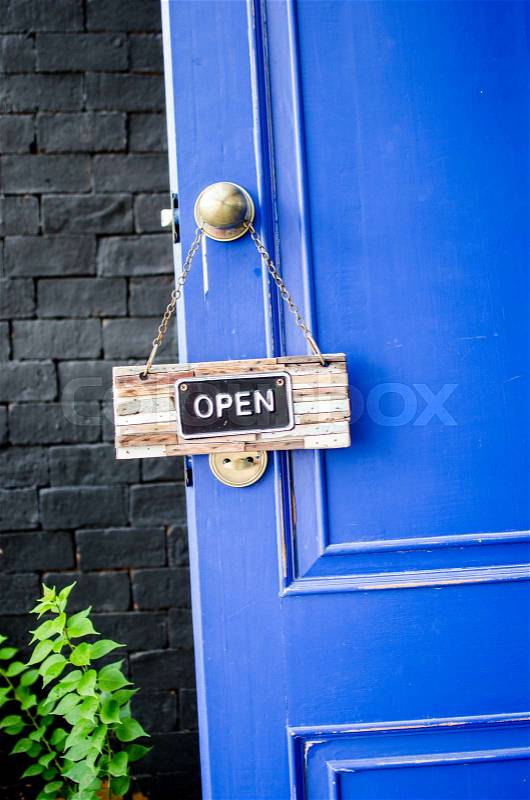 Open label hanging on blue door in garden, stock photo