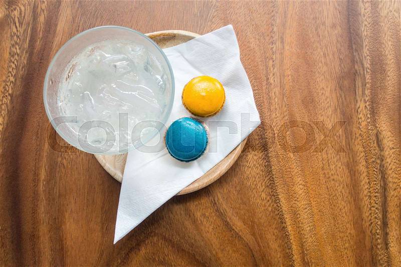 Welcome drink set with fresh ice-water, blue and orange colors magaroons and white napkin in wooden tray on wooden table, stock photo