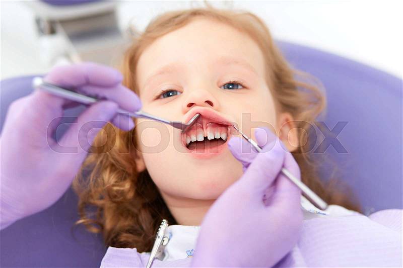 Hands of unrecognizable pediatric dentist holding lip up and making examination of cute little girl in chair in a hospital. Dentist and child in cabinet. Dentist office, stock photo