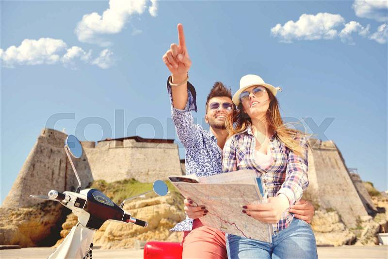 Examining map together. Beautiful young loving couple sitting on scooter together and examining map while woman pointing it and smiling, stock photo