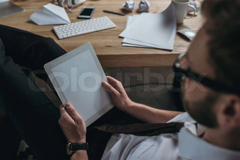 Young businessman using digital tablet while sitting at workplace, stock photo