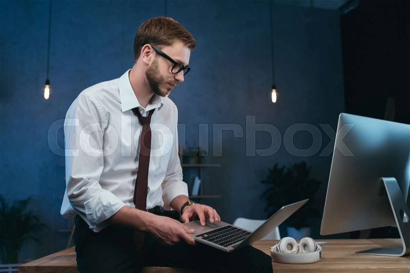 Young businessman in formal wear working on laptop at modern office, stock photo