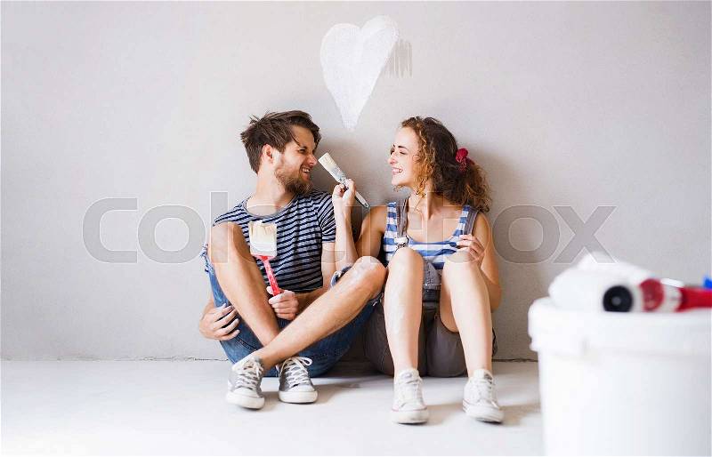 Beautiful young couple in love having fun, painting walls of their new house. Home makeover and renovation concept, stock photo