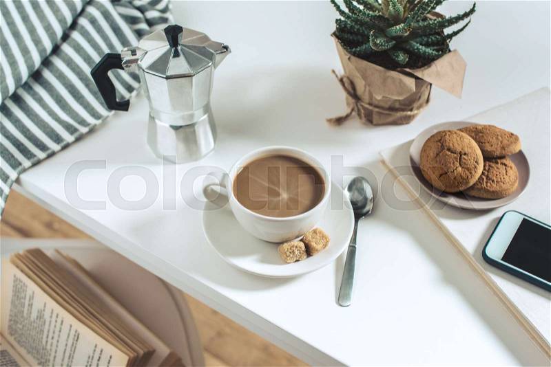 Coffee cup with cookies and potted plant with smartphone on tabletop, stock photo