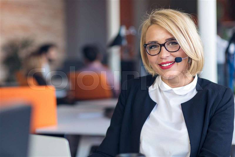 Customer service representative at work. Beautiful young woman in headset working at the computer and smiling while sitting at her working place in office, stock photo