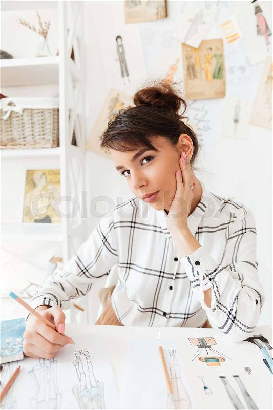 Portrait of a young woman designer drawing sketches at ter workplace in studio, stock photo