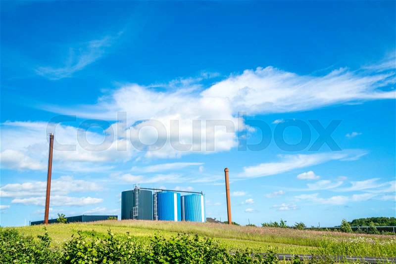 Industrial factory with large silos in blue colors and two high chimneys on a field in the summer, stock photo