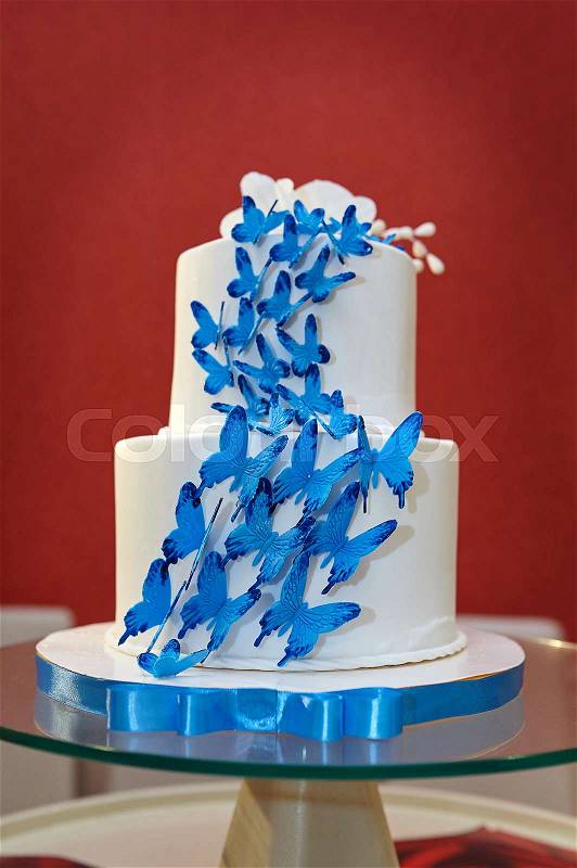 Two-tier wedding cake with blue butterflies on glasses table, stock photo