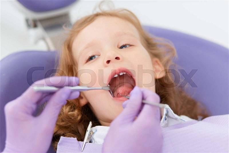 Close-up shot of little girl sitting at unrecognizable dentist while she making oral examination in hospital. Dentist and child in cabinet. Little girl sitting in the dentists office, stock photo
