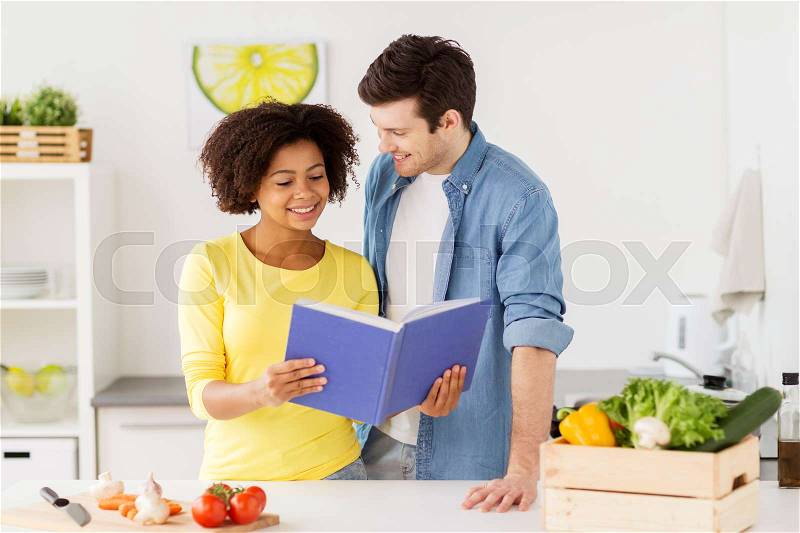 People, cooking food and healthy eating concept - happy couple with cookbook and vegetables at home kitchen, stock photo