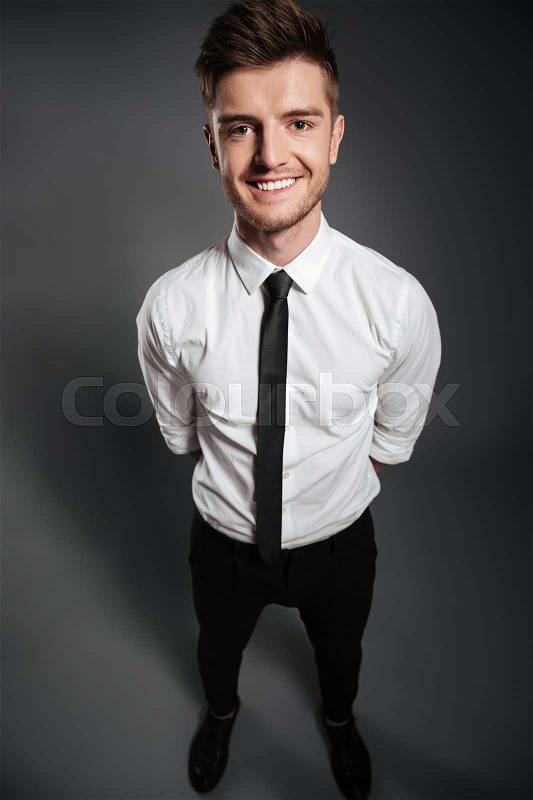 Top view full length portrait of a happy handsome man in formalwear standing and looking at camera isolated over grey background, stock photo
