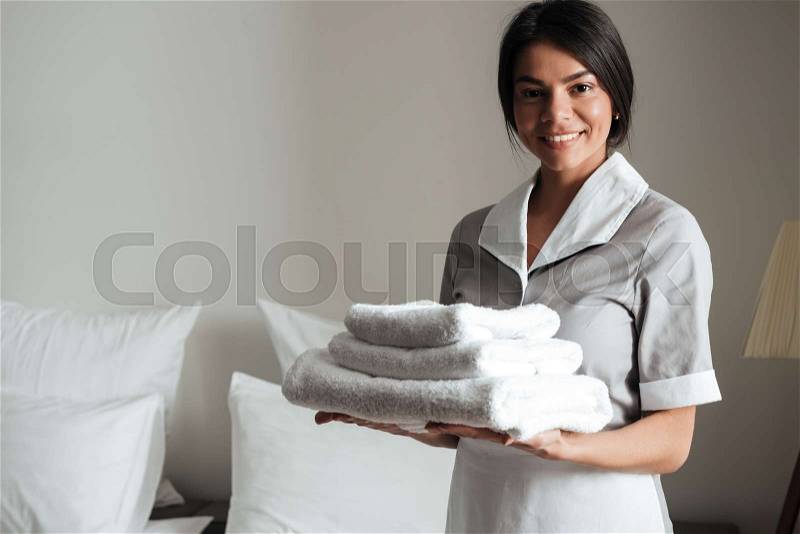 Portrait of a smiling hotel maid holding fresh clean folded towels for the room, stock photo