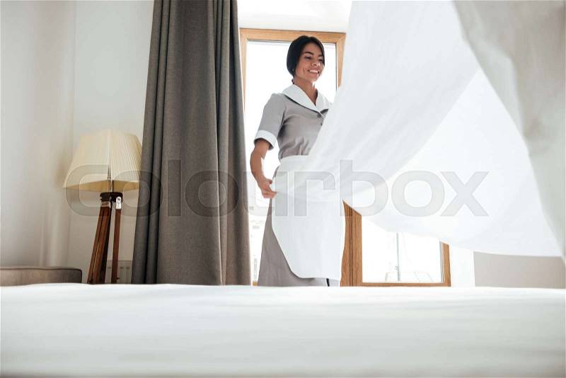 Young hotel maid changing bed sheets, stock photo