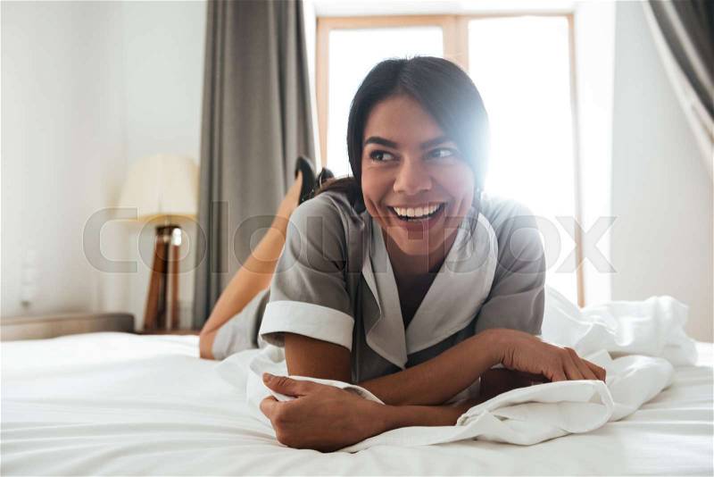 Smiling young hotel maid lying on a bed, stock photo