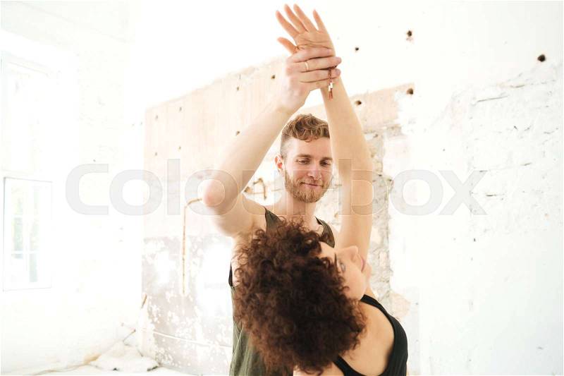 Male yoga instructor helping african woman to do yoga stretches in a studio, stock photo