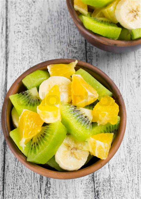Fruit salad with kiwi, banana and orange in the bowl on the wooden board, stock photo