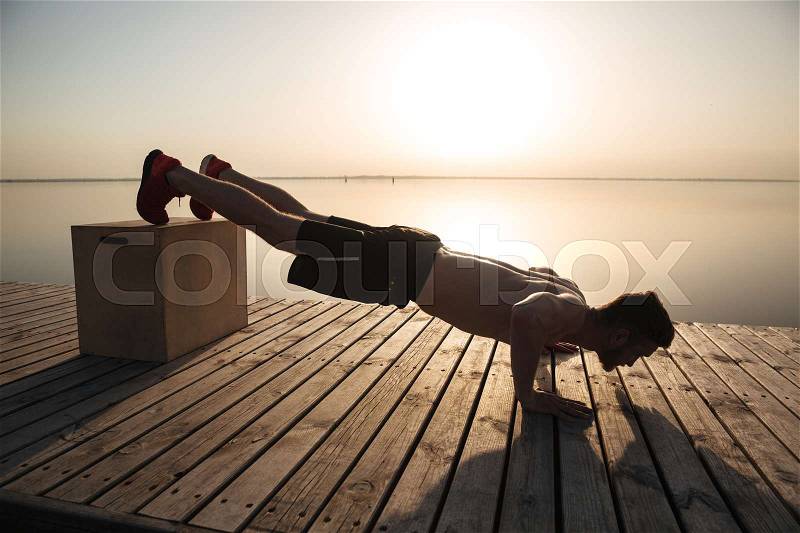 Young healthy man doing push-ups with special equipment on the beach in the morning, stock photo