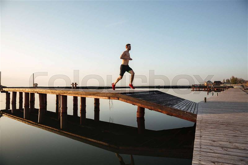 Image of handsome young sportsman running at the beach. Looking aside, stock photo