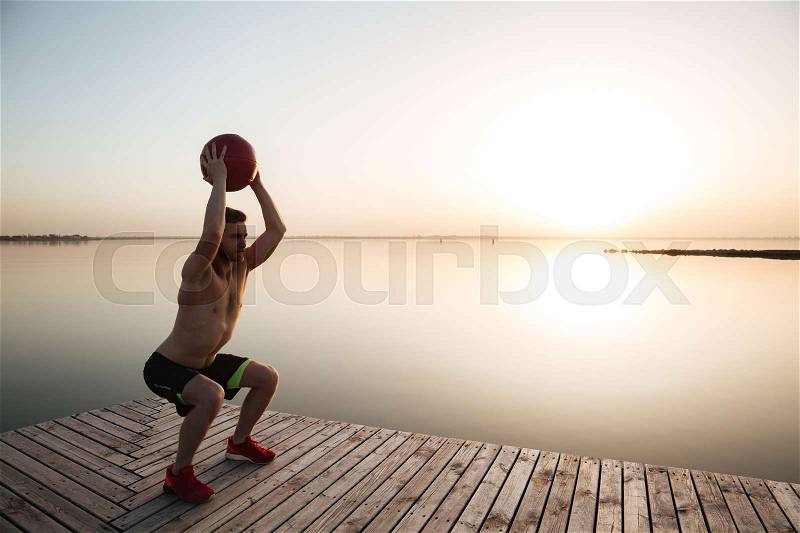 Photo of concentrated young sportsman make sport exercises with ball at the beach. Looking aside, stock photo