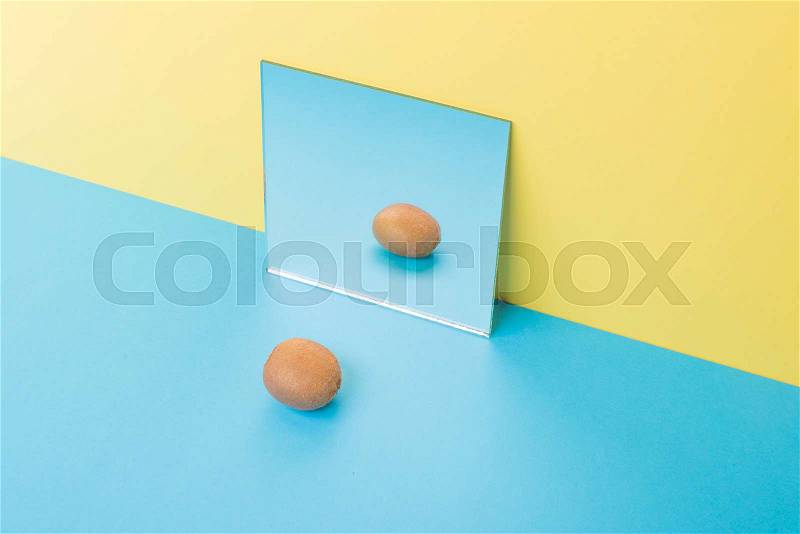 Image of kiwi on blue table isolated over yellow background near mirror, stock photo
