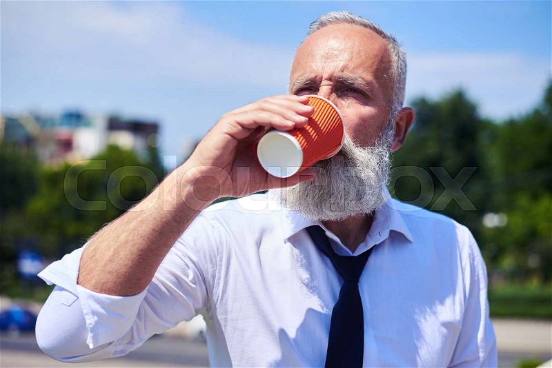 Close-up of man with poker face drinking coffee and enjoying panorama of city, stock photo