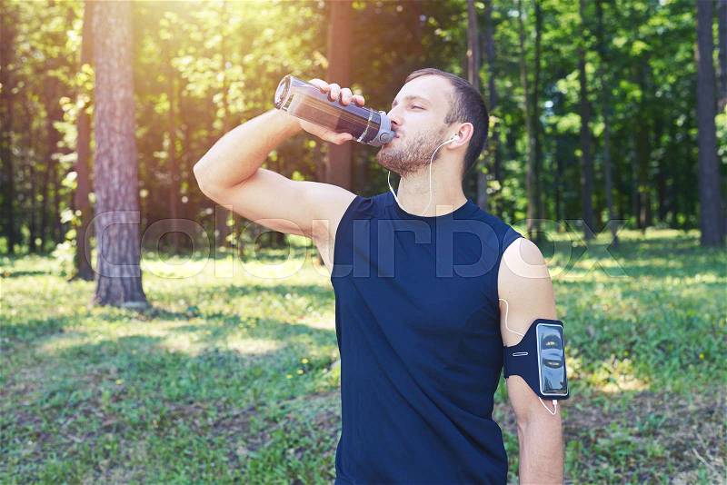 Mid shot of a male drinking water, wearing sport cloth; listening to music. Having strong muscles, in good shape, stock photo