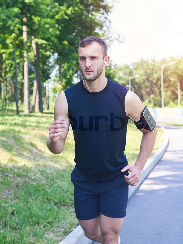 Vertical of good-looking man running in park while listening to music, stock photo