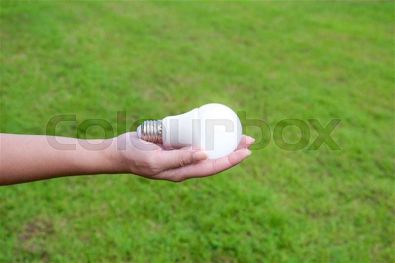 Led bulb with lighting in woman hand with grass background for saving energy concept, stock photo