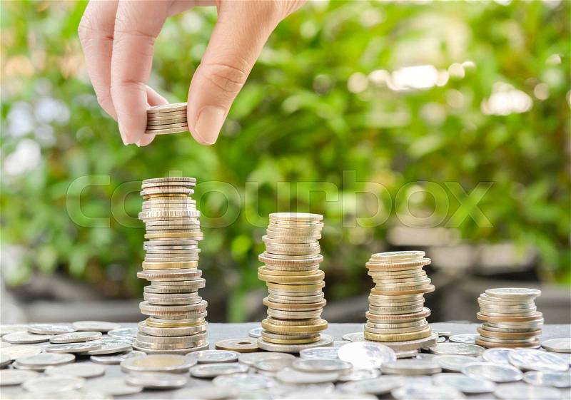 Woman hand putting coin to growing coins stacks with sun light - Concept of saving money, stock photo