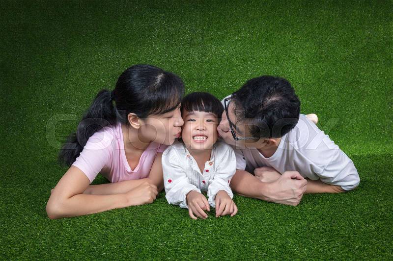 Happy Asian Chinese parents and daughters lying on the grass at outdoor park, stock photo