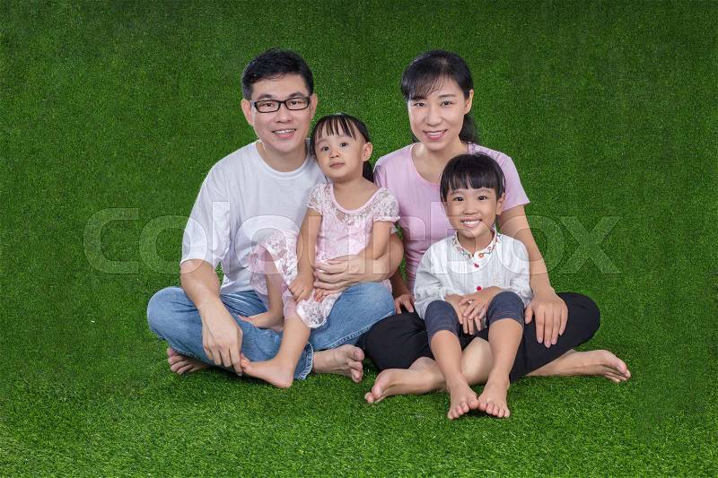 Happy Asian Chinese parents and daughters sitting on the grass at outdoor park, stock photo
