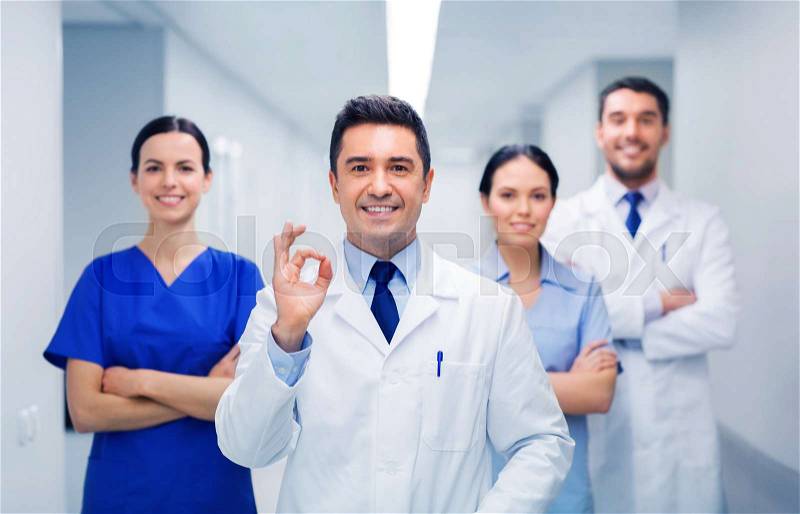 Clinic, profession, people, health care and medicine concept - group of happy medics or doctors at hospital corridor showing ok hand sign, stock photo