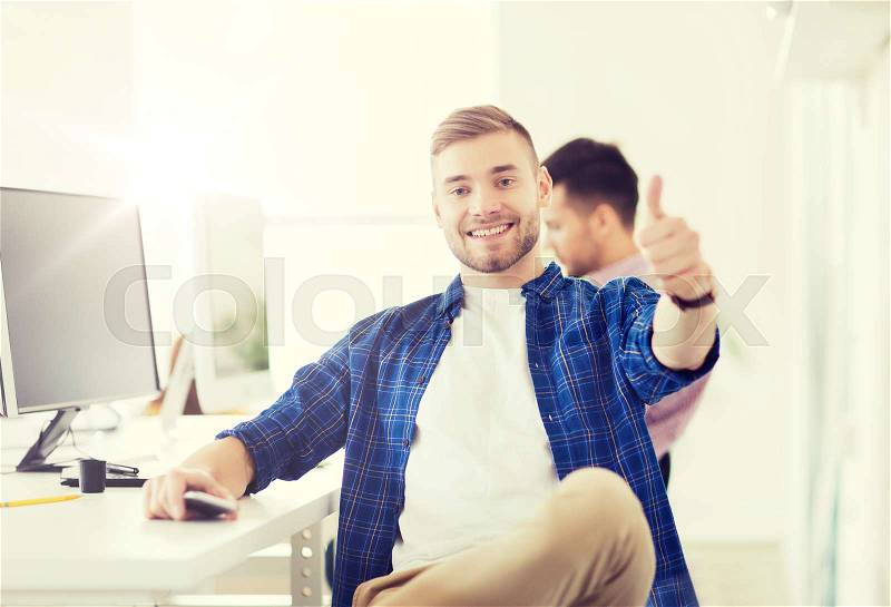 Business, technology, education and people concept - happy young creative man or student with computer at office at office showing thumbs up, stock photo