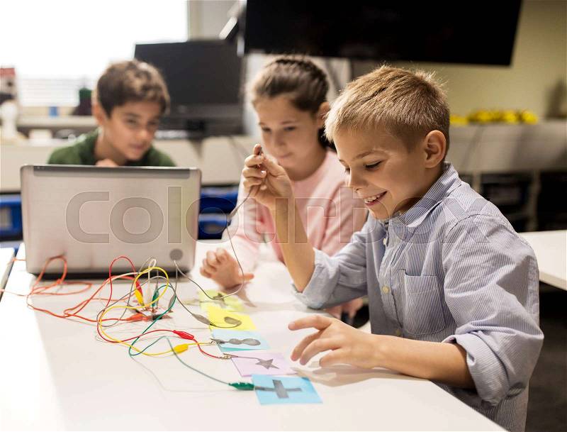 Education, children, technology, science and people concept - group of happy kids with laptop computer playing with invention kit at robotics school lesson, stock photo
