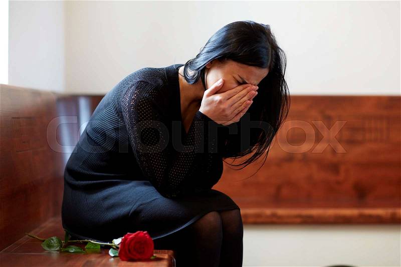 People, grief and mourning concept - crying woman with red rose sitting on bench at funeral in church, stock photo