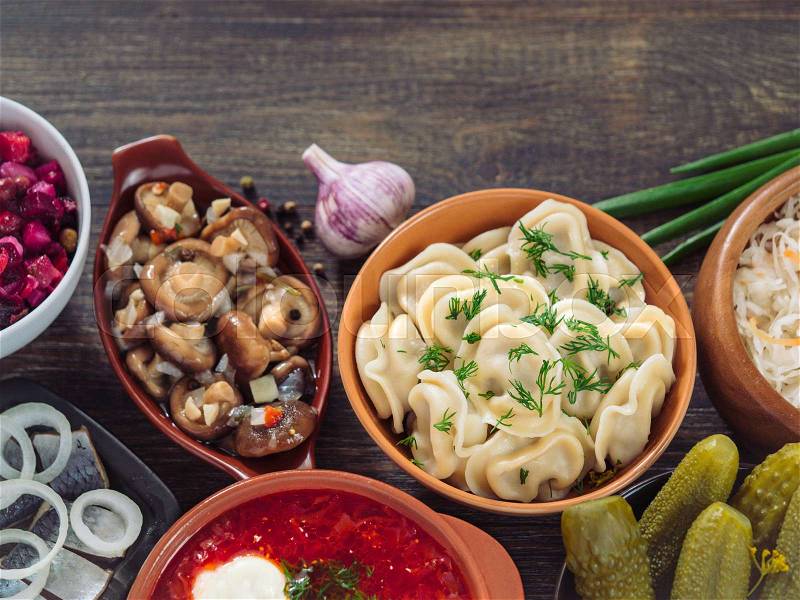 Russian food with copy space. Assortment dishes of Russian cuisine - borscht, pelmeni, herring, marinated mushrooms, salted cucumbers, vinaigrette, sauerkraut and pancakes. Top view or flat lay, stock photo