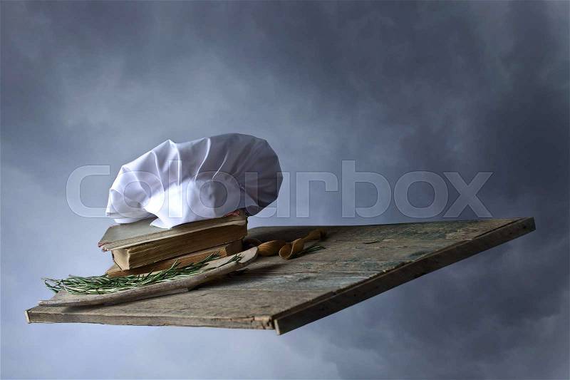 Old culinary books , chef hat and wooden spoons . Kitchen accessories on the old wooden table in the sky, stock photo