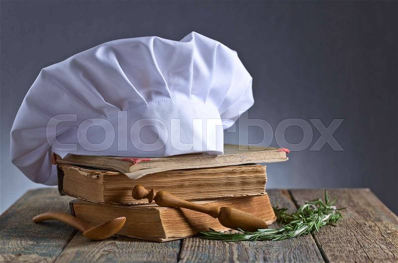 Old culinary books , chef hat and wooden spoons . Kitchen accessories on the old wooden table , stock photo