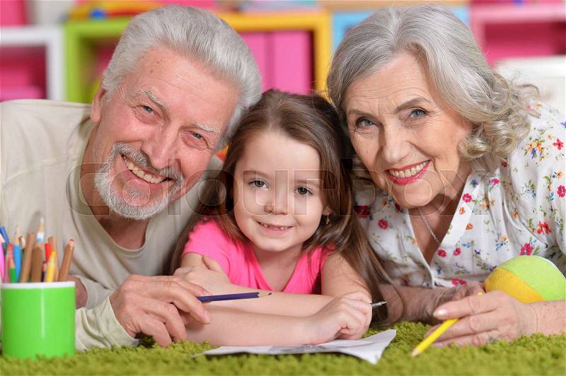 Grandparents playing with their grandaughter while lying on floor, stock photo
